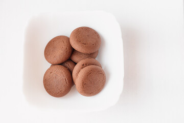 Round brown chocolate flavored cookies served in a white bowl closeup