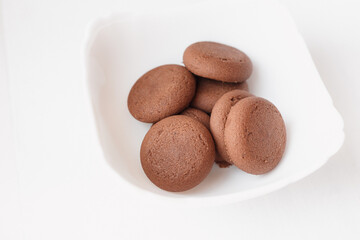 Round brown chocolate flavored cookies served in a white bowl closeup
