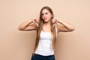 Teenager blonde girl over isolated background showing thumb down