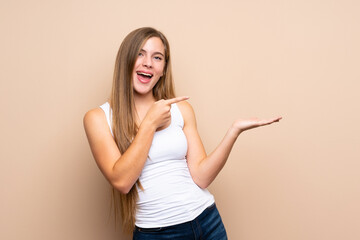 Teenager blonde girl over isolated background holding copyspace imaginary on the palm to insert an...