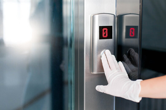 Female hands in medical protective gloves pressing elevator button. Young woman touches lift buttons. Disease prevention during quarantine, hygiene. Close up.