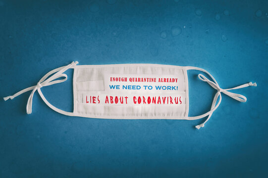 ENOUGH QUARANTINE ALREADY. We need to work. Lies About Coronavirus. Disposable respiratory mask on a blue grunge background with pandemic inscriptions.