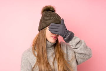 Young teenager girl with winter hat over isolated pink background covering eyes by hands