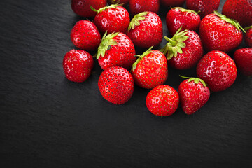 A pile of strawberries background. Strawberries on a dark slate stone. Background image with copy space. Healthy berries.