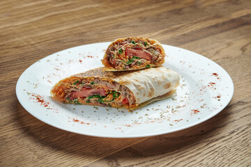 Classic oriental shawarma roll with minced meat, tomatoes, herbs and cheese on a white plate on a wooden background. Tasty kebab