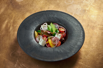 Classic greek salad with red onion, feta cheese, cucumber, bell pepper in a black plate on a copper, metal background. Close up view.