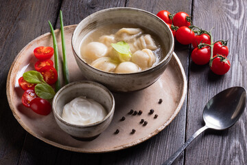 Boiled meat dumplings served with sour cream and cherry tomatoes on black background . Traditional Russian pelmeni. Top view.