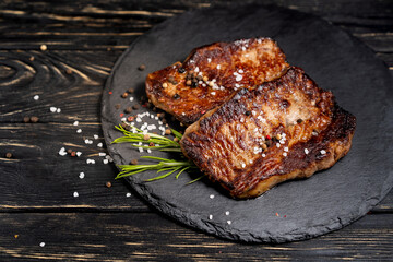 juicy piece of fried meat lies on a stone plate against a black wooden table