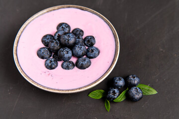 Tasty fresh blueberry yogurt shake dessert in ceramic bowl standing on black dark table background.