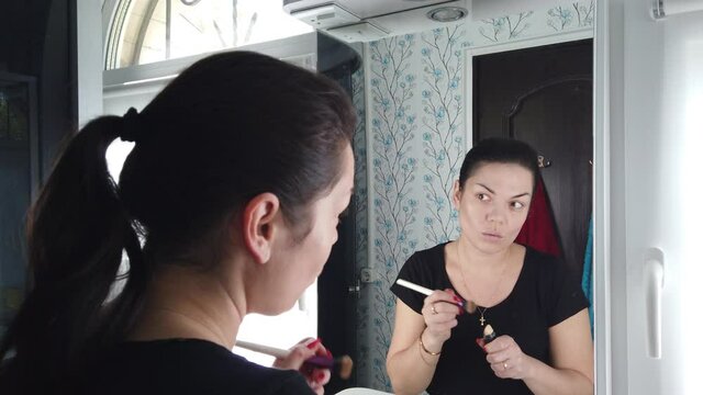 Pretty brunette woman doing makeup in front of mirror in bathroom