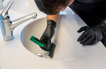 professional cleaner removing lime scale from a ceramic bathroom sink with a diamond blade scraper