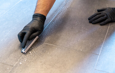 close up of professional cleaner cleaning grout with a brush blade and foamy soap on a gray tiled...
