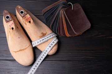Leather samples for shoes and wooden shoe last on dark wooden table.