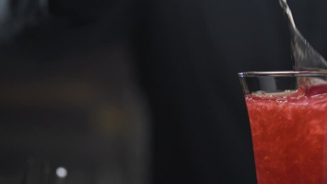 Making Strawberry Rossini Cocktail. Close up bartenders hands pouring champagne into a glass with crushed strawberries, then put a strawberry flower on a skewer on the top of glass. Rotating