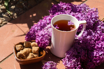 white porcelain cup with tea and among flowering branches of lilac