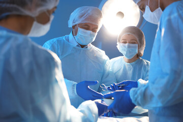 Team of professional doctors performing operation in surgery room - obrazy, fototapety, plakaty
