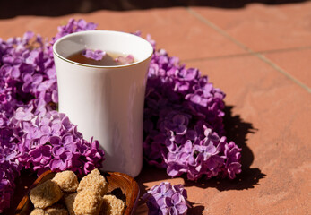 Fototapeta na wymiar white porcelain cup with tea and among flowering branches of lilac