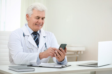 Senior doctor with smartphone at table in office