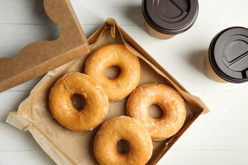 Delicious donuts in box and coffee on white table, flat lay