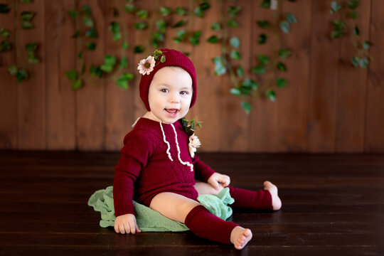 a cheerful 12 month old girl is sitting in a beautiful outfit smiling on a dark wooden background