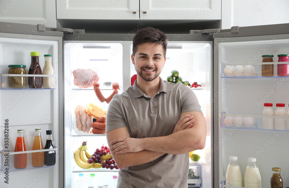 Wall mural Young man near open refrigerator in kitchen