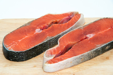 Close-up of two slices of raw red fish salmon on wooden board isolated on white background