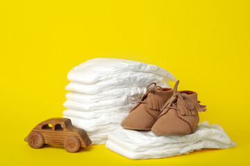 Fototapeta na wymiar Diapers, toy car and baby shoes on yellow background