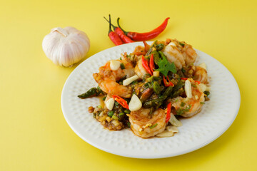 Stir-fried shrimp with chilli with garlic and chilli and spoon and fork with yellow background.