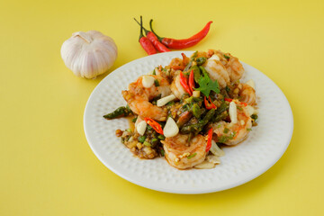 Stir-fried shrimp with chilli with garlic and chilli and spoon and fork with yellow background.