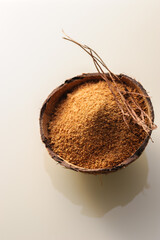 natural granulated coconut sugar in a coconut shell on a light background, view from above