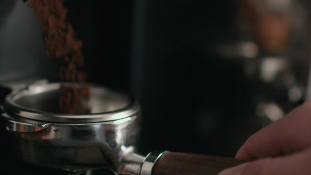 Slow motion handheld shot of grinding coffee beans in portafilter closeup
