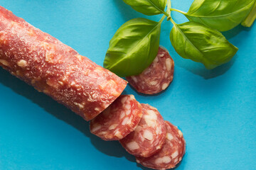 Cold smoked, dried sausage close up. Top view, blue background. Basil