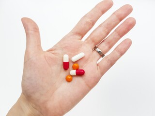 Three white-red capsules and two orange tablets on the palm of your hand on a white background.