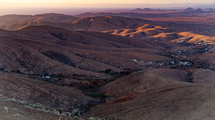 Fototapeta na wymiar Letztes Sonnenlicht fällt auf eine hügelige Wüstenlandschaft mit Bergen, Tälern und verstreuten Siedlungen