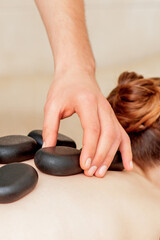 Obraz na płótnie Canvas Back massage of woman with black hot stones by male massage therapist.