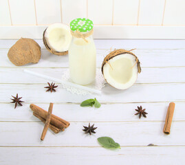 Fototapeta na wymiar Coconut milk, in a glass bottle on a white background.Exotic fruit, coconut on the table.Spices of cinnamon, star anise and mint, for a drink.