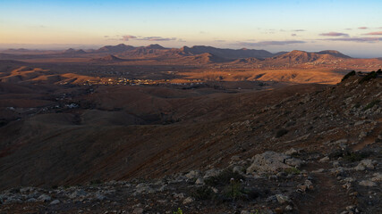 Letztes Sonnenlicht fällt auf eine hügelige Wüstenlandschaft mit Bergen, Tälern und Siedlungen