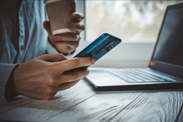 Young adult sitting in freelance home office with black laptop and phone