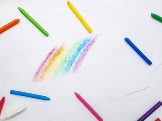 Colored wax crayons on white paper. A rainbow drawn by children's hands.