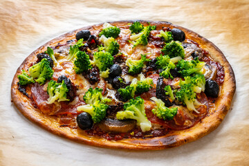 Pizza with broccoli and black olives on baking paper