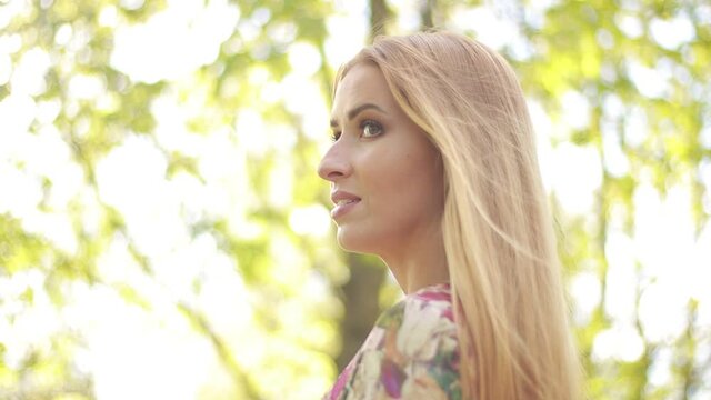 Video clip, blur effect and light fler, a young blonde woman with long hair in a long dress walks in a blossoming apple orchard on a sunny day in spring.