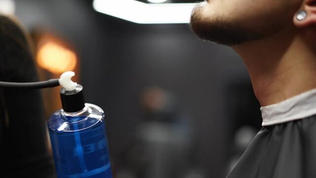Barber sprays parfume on client in barbershop after haircut and styling. Hairdresser using old fashined sprayer with toilet water in hair salon after customer's beard shaving. Vintage cologne bottle.