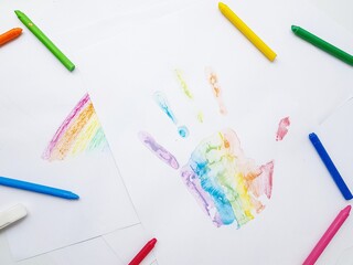 Colored wax crayons. A handprint on a white sheet of paper.