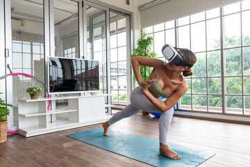 Young good looking woman practising yoga use VR technology attending online class at home