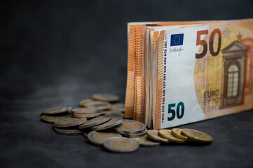 a stack of 50 euro money and many euro coins on a dark background