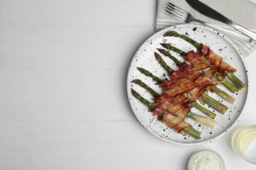 Oven baked asparagus wrapped with bacon on white wooden table, flat lay. Space for text