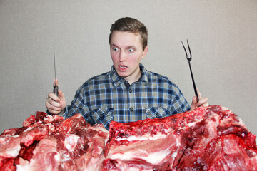 A man eagerly looks at raw meat. A man with a knife and a fork. A lot of fresh meat. Man and raw...