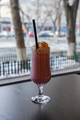Fresh milk strawberry shake in glass goblet with tube and milk cream, with window as background, centered composition