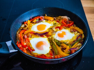 Shakshuka - fried eggs with vegetables in frying pan
