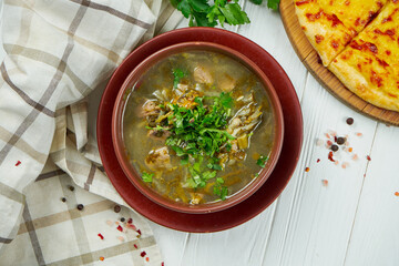 Top view on tasty Chakapuli - traditional Georgian stew with lamb chops or veal, onions, tarragon leaves, cherry plums or tkemal in ceramic plate. Wooden background